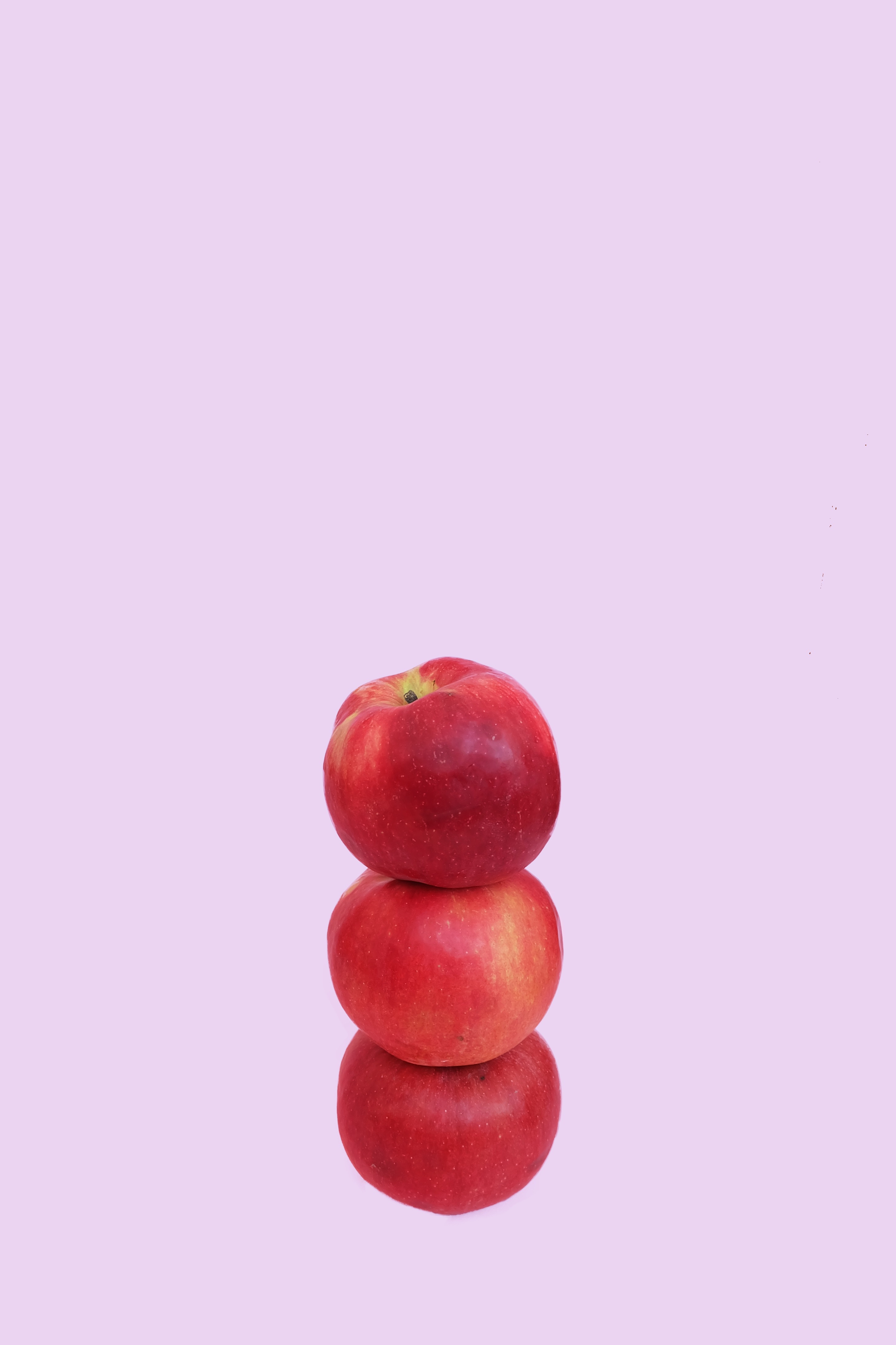 A purple background, in front are three red apples stacked on top of each othter
