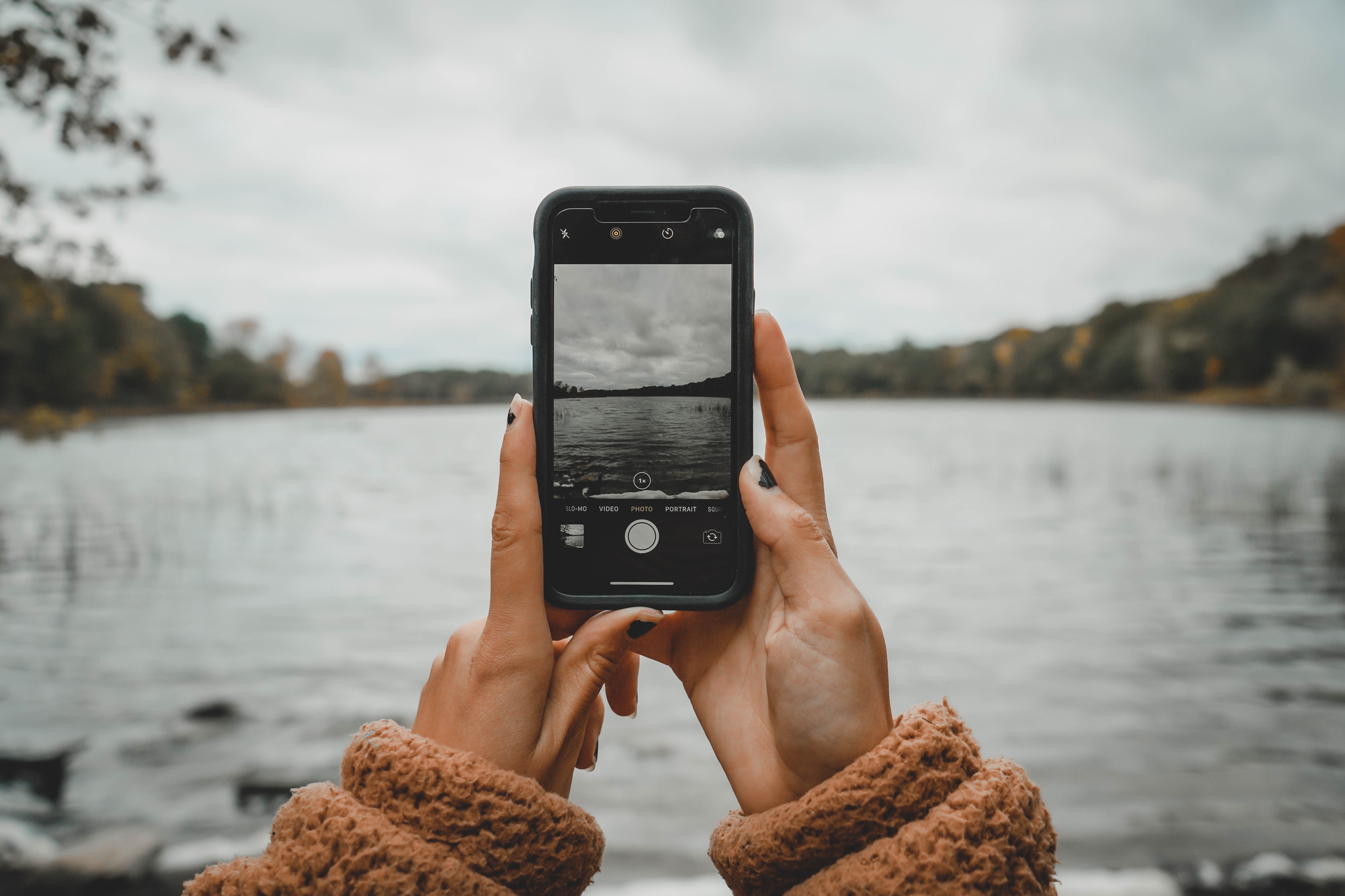 Picture of someone holding a smart phone taking a photo of a lake.