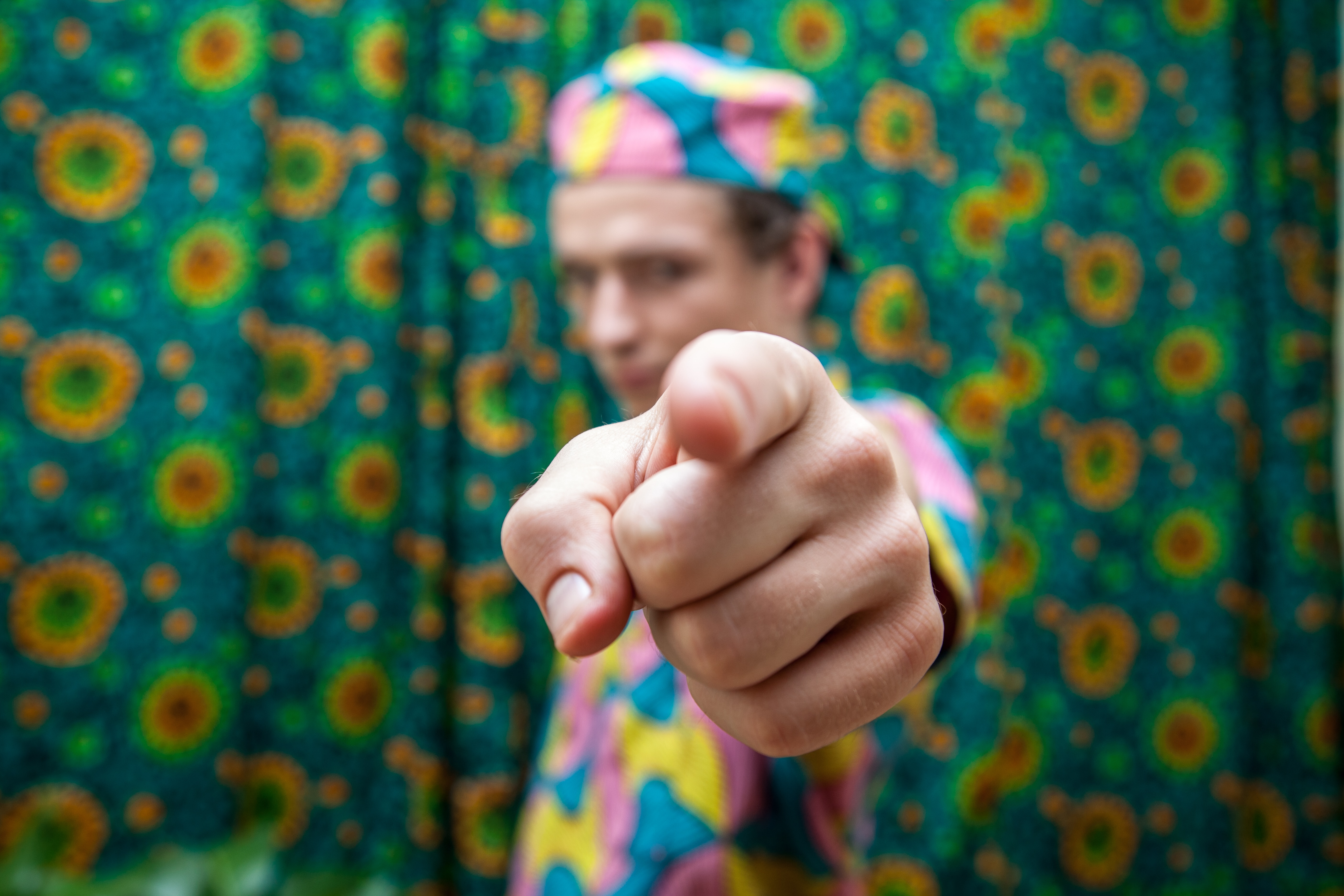 A person pointing a finger towards you, the person is blurred. The finger is focused and close