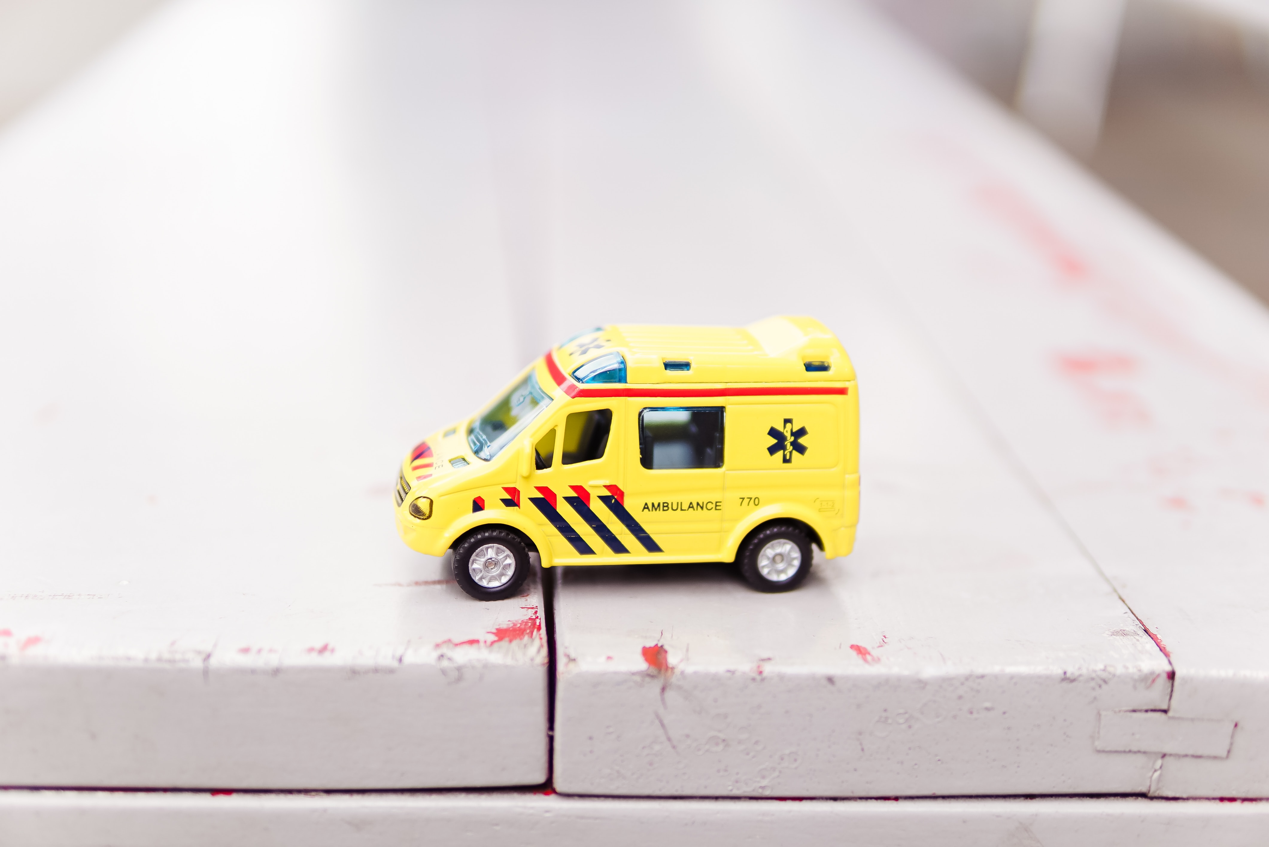 A toy ambulance on top of a white wooden bench