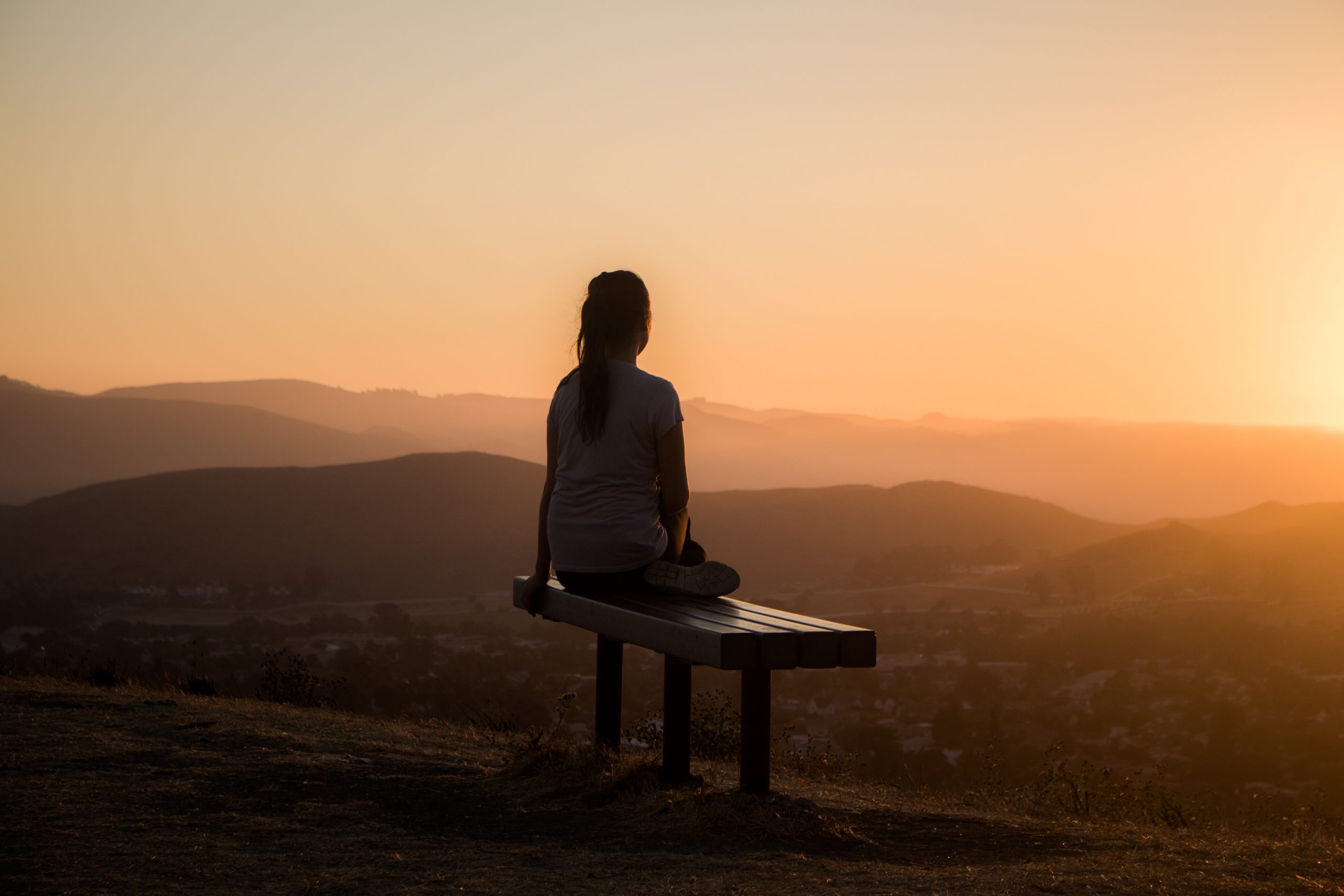 Woman setting with her back towards you with her back turend, watching beautiful sunset.