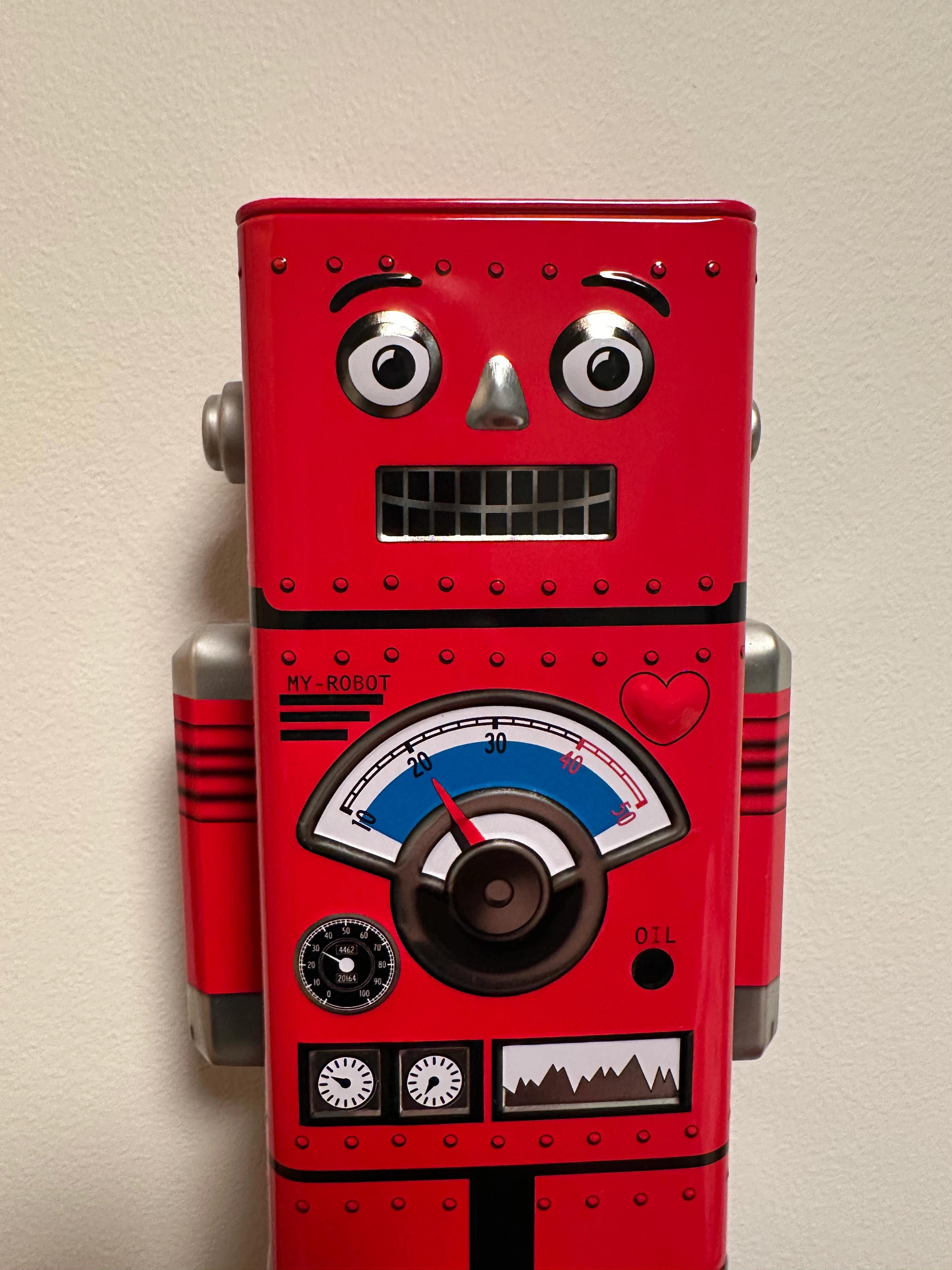 Picture of a red metallic robot in front of a white wall.